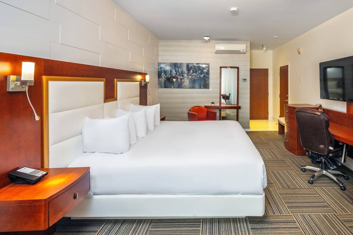 A hotel room with a large bed, a desk with a chair, a television, and a painting on the wall.