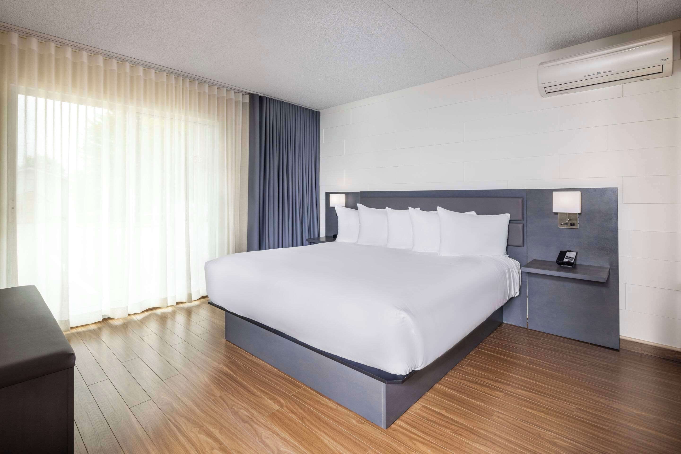 Ein modernes Hotelzimmer mit einem großen Bett, einem Nachttisch mit Lampe und einer fest installierten Klimaanlage.