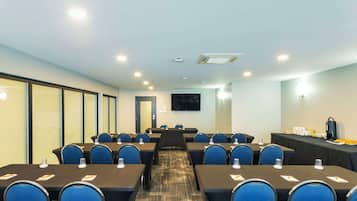 A conference room with tables and chairs, a projector screen, and a buffet table with food and drinks.