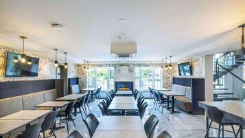 A modern restaurant with marble flooring, black chairs, and tables arranged around a central fireplace.