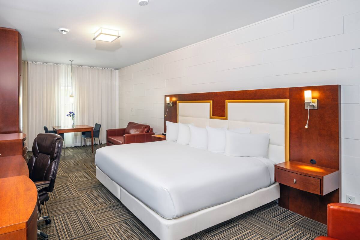 A hotel room with a large bed, a desk, a chair, and a small table.