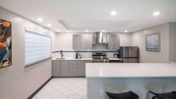 A modern kitchen with grey cabinets, a stainless steel range hood, and a large island with bar stools.