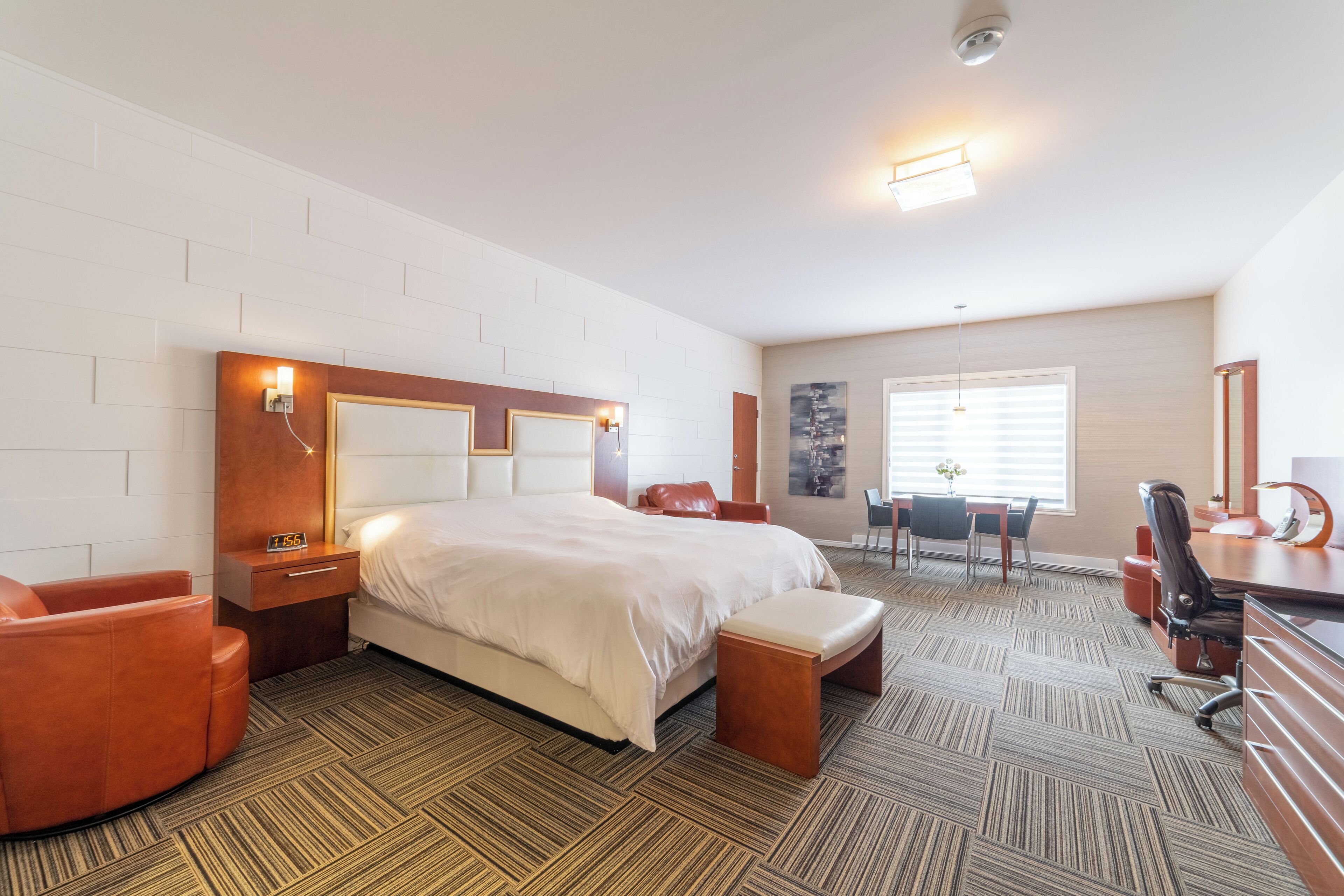 Quarto de hotel com uma cama grande, uma escrivaninha, uma cadeira e um pequeno espaço de estar.