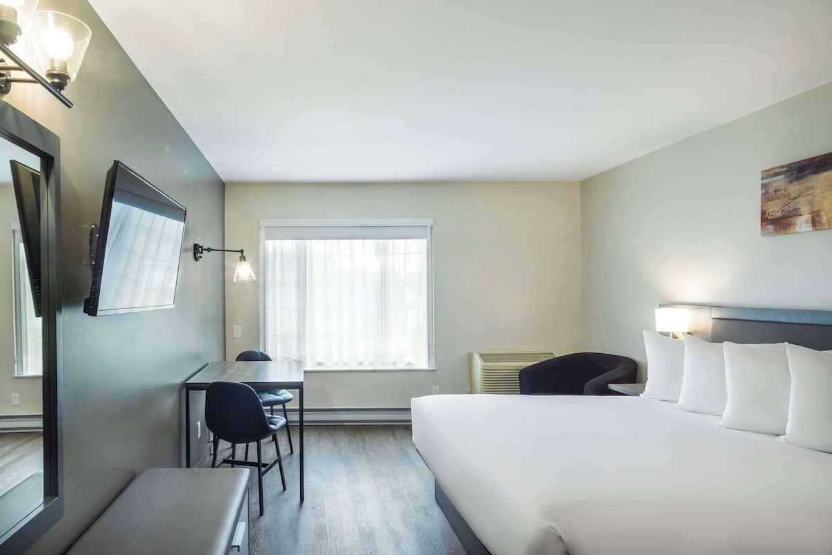 A hotel room with a bed, a desk, a chair, a TV, and a window with curtains.