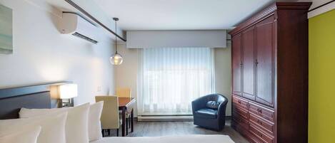 Une chambre d’hôtel avec un grand lit, un bureau avec une chaise, une armoire et une fenêtre avec des rideaux.