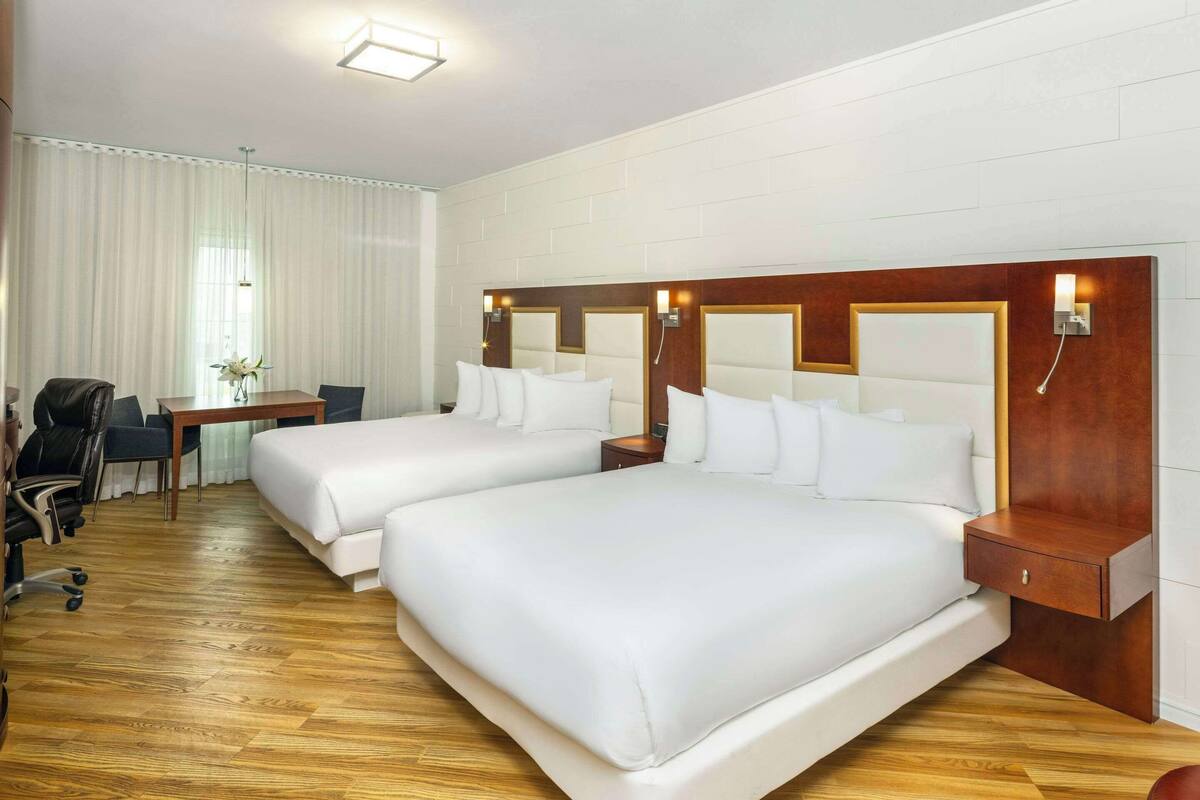 A hotel room with two beds, a desk, a chair, and a small table.