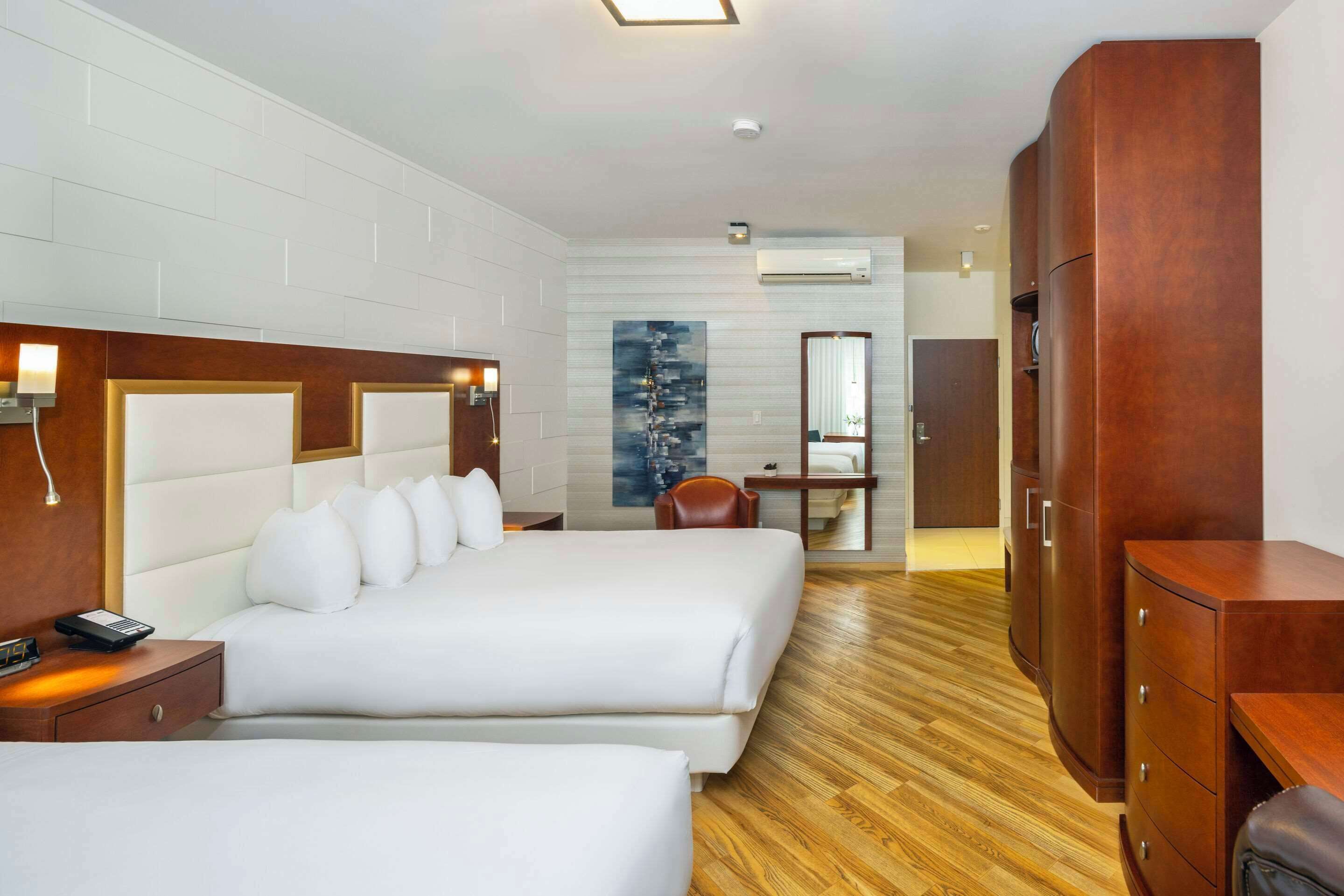 Ein Hotelzimmer mit zwei Betten, Holz-Kopfteilen, einem Schreibtisch, einem Stuhl, einem Kleiderschrank und einem Gemälde an der Wand.
