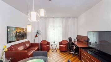 A modern living room with a leather sofa, red armchairs, a glass coffee table, a TV, and a painting on the wall.