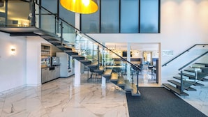 Un hall d’hôtel moderne avec un sol en marbre, un escalier en verre et un espace bar.