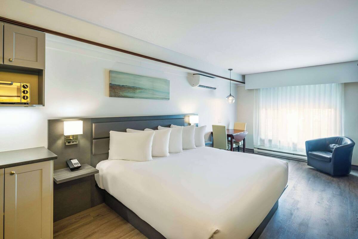 A hotel room with a large bed, bedside tables, a desk, a chair, and a window with curtains.