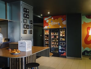 Un vestíbulo de hotel moderno con un mostrador de recepción, una caja para llaves y una zona comercial con exhibiciones de comida y bebida.