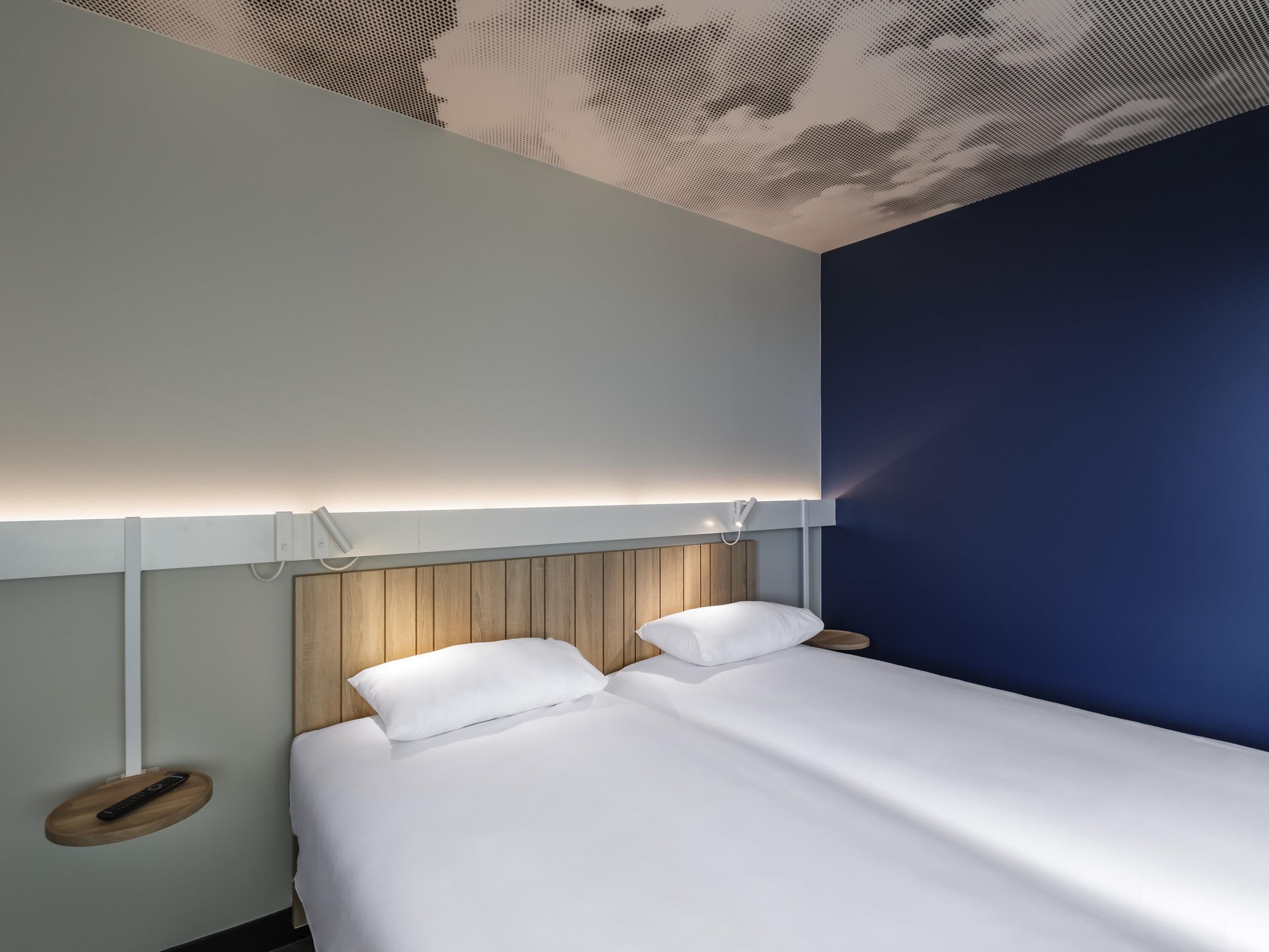 Una habitación de hotel moderna con cama, mesitas de noche y un diseño de techo original.