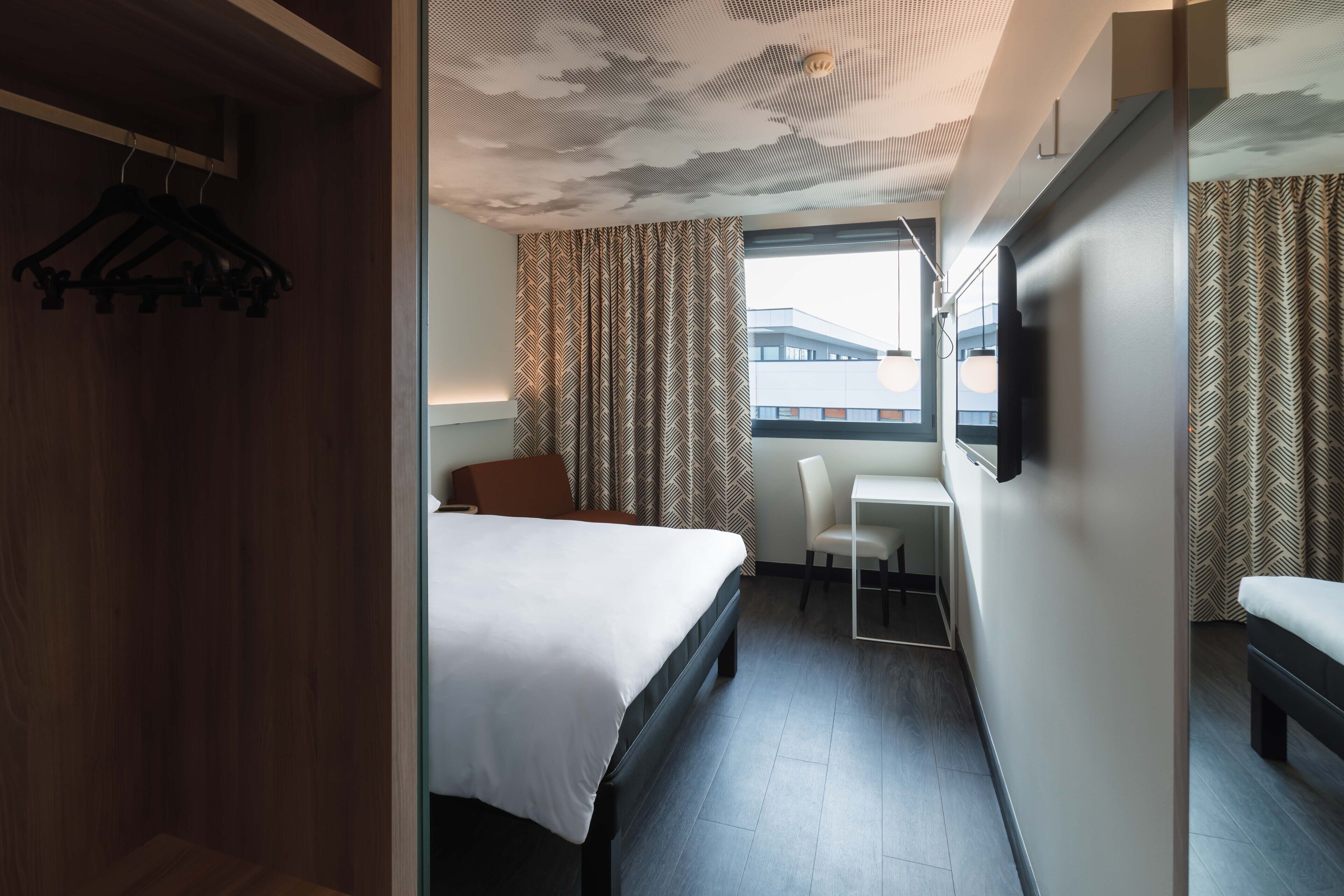 Una habitación de hotel con cama, escritorio, silla y televisor en la pared.