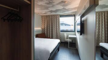 Una habitación de hotel con cama, escritorio, silla y televisor en la pared.