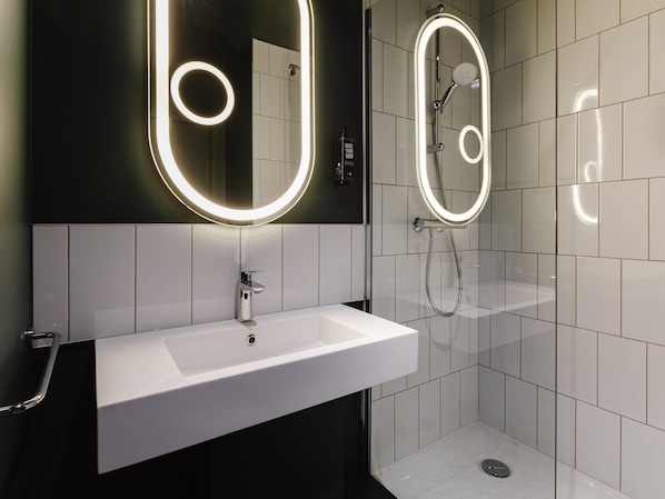 A modern bathroom with a white sink, a mirror with illuminated edges, and a shower with a handheld showerhead.