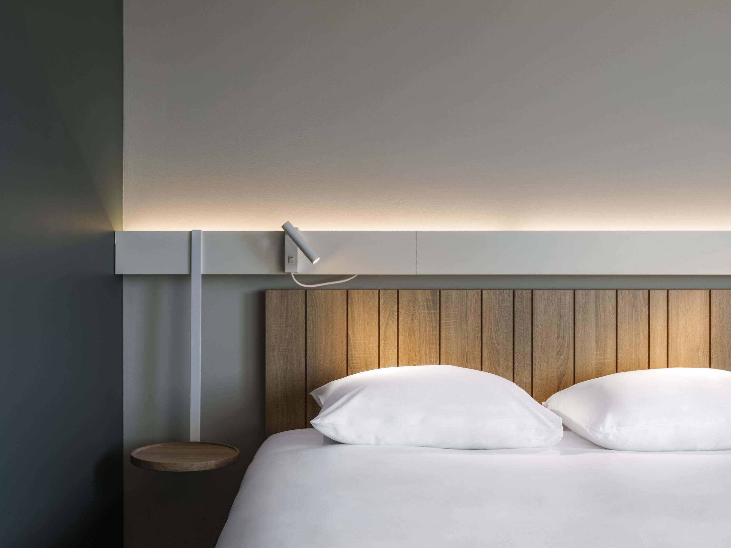 A modern bedroom with a wooden headboard, a bedside table, and a wall-mounted light fixture.