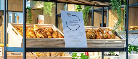 Una vitrina de pastelería con cruasanes y bollería en estantes, un cartel con texto y una pequeña planta.