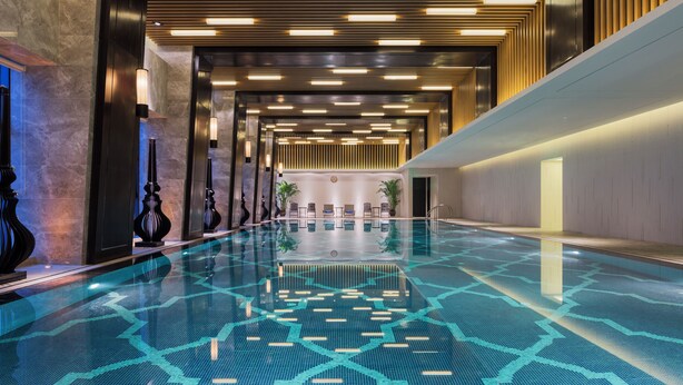 A spacious indoor swimming pool with a geometric tile pattern, surrounded by modern lighting fixtures and a reception area. - Nanjing Wanda Realm Hotel (Nanjing)