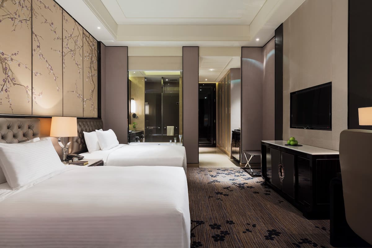 A hotel room with two beds, a television, a desk, and a large decorative panel on the wall.