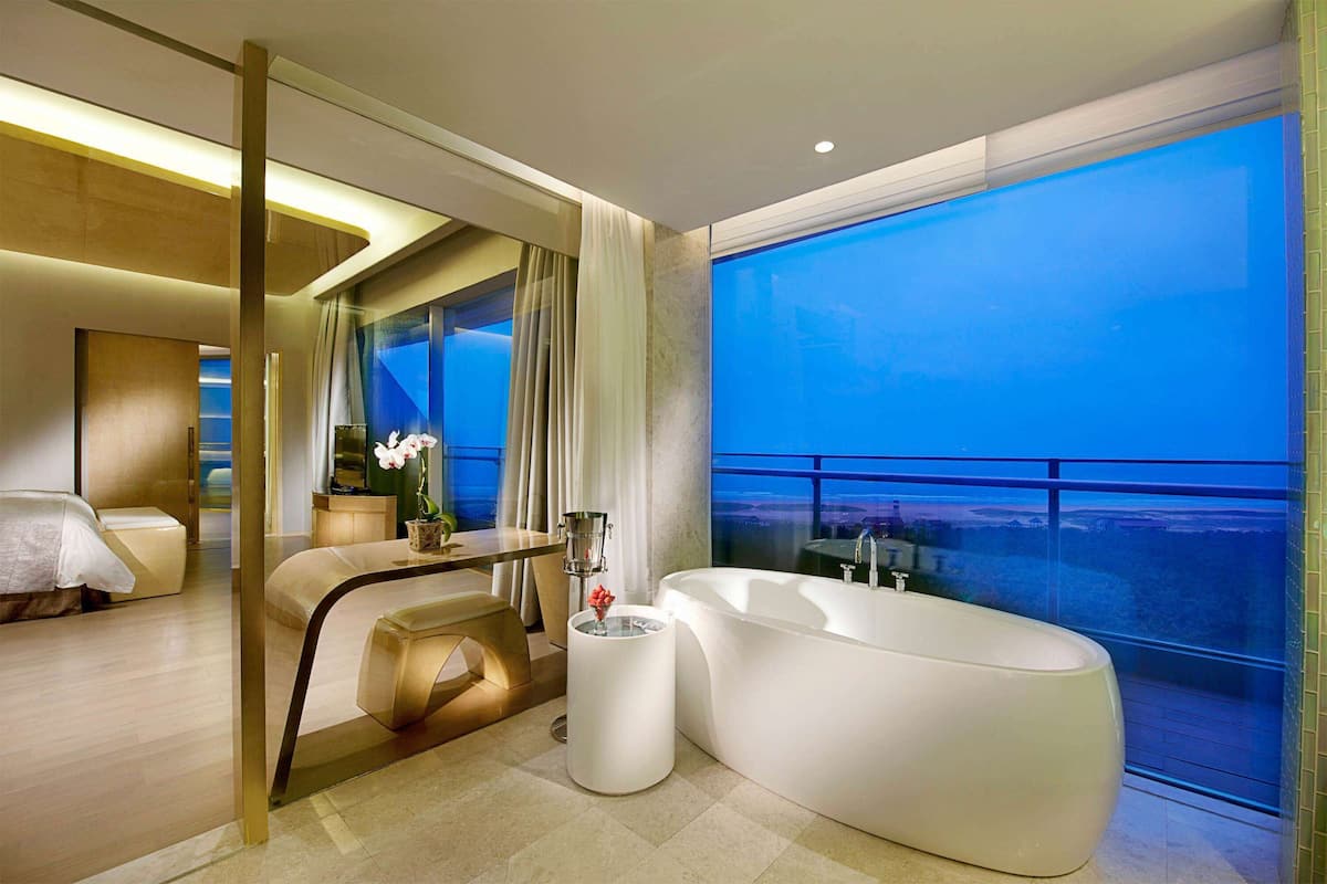 A modern bathroom with a large bathtub, a vanity, and a large window with a view of the ocean.