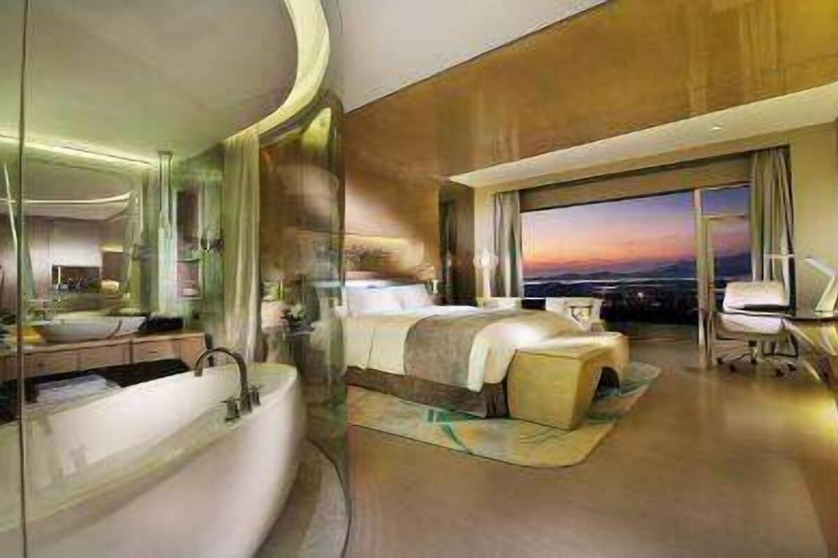 A modern hotel room with a large bed, a separate sitting area, a large window with a view, and a separate bathroom.