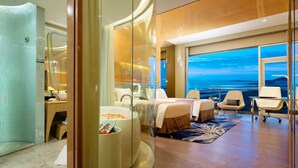 Una habitación de hotel moderna con una cama grande, una zona de estar con pared de vidrio y vistas al océano, así como una bañera.