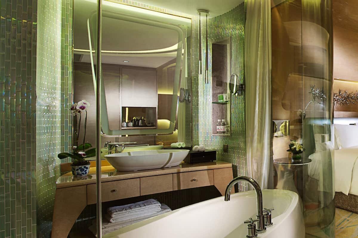 A modern bathroom with a large bathtub, a sink, and a mirror. There is a glass partition and a small table with toiletries.
