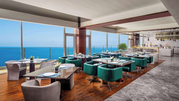 Un restaurante moderno con mesas y sillas, amplias ventanas con vista al océano y una zona de bar.