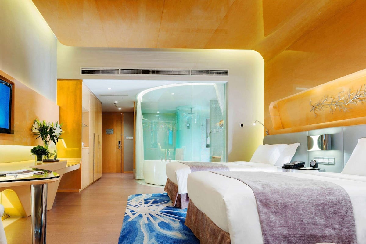 A hotel room with a bed, a desk, a bathroom, and a shower area.