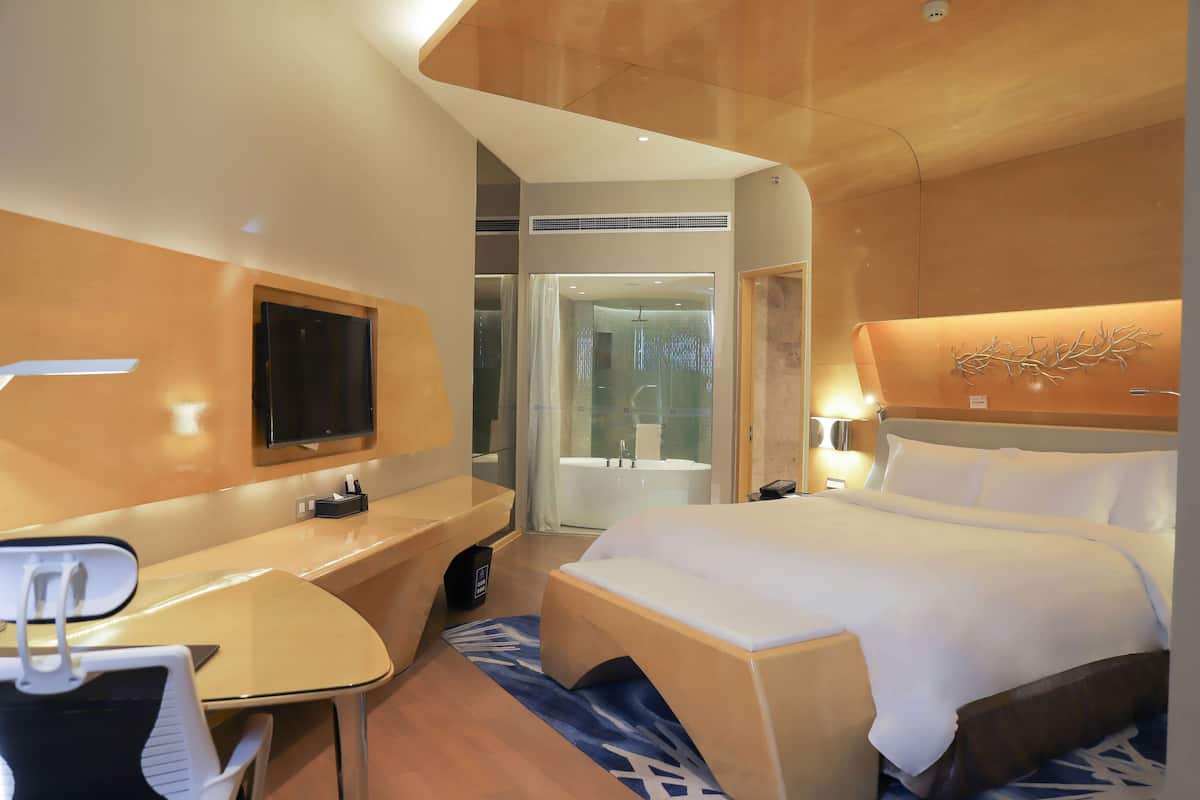 A hotel room with a bed, desk, chair, and a TV.