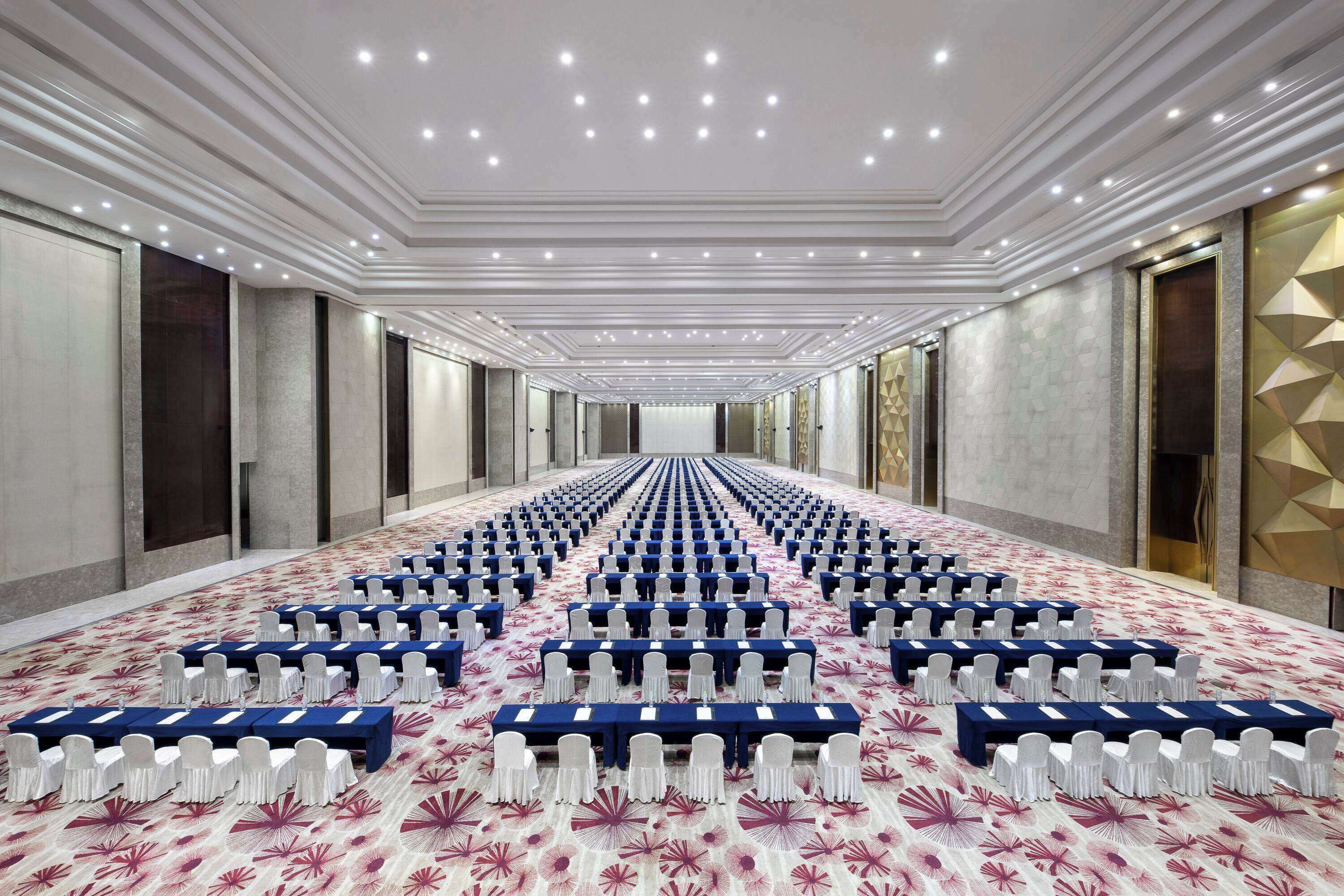 Une salle de conférence avec des rangées de tables et de chaises, une moquette à motifs et un design de plafond moderne.