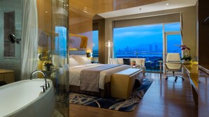 Una habitación de hotel moderna con una cama grande, un área de descanso, una bañera y vistas a la ciudad.