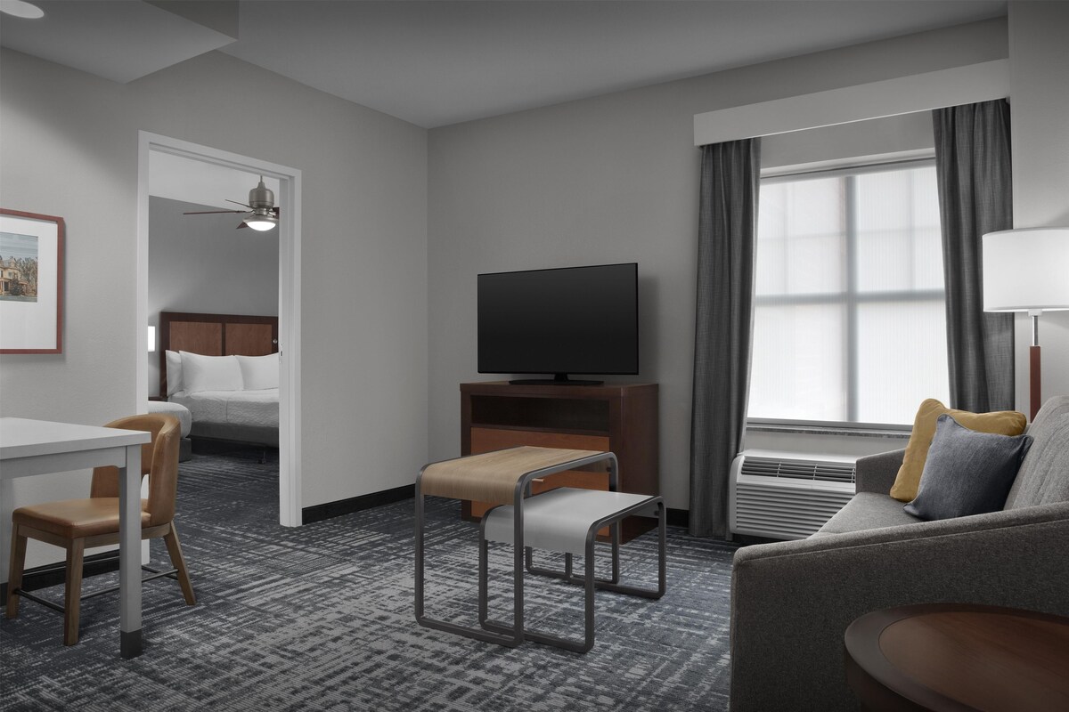 Habitación de hotel con cama, televisor, sofá, mesita y silla.