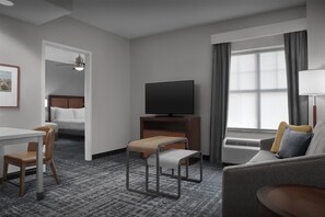 A hotel room with a bed, a TV, a sofa, a small table, and a chair.
