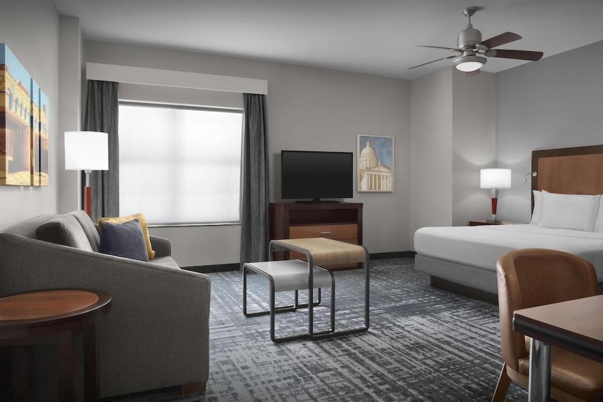 Una habitación de hotel con cama, sofá, escritorio, televisor y ventilador de techo.