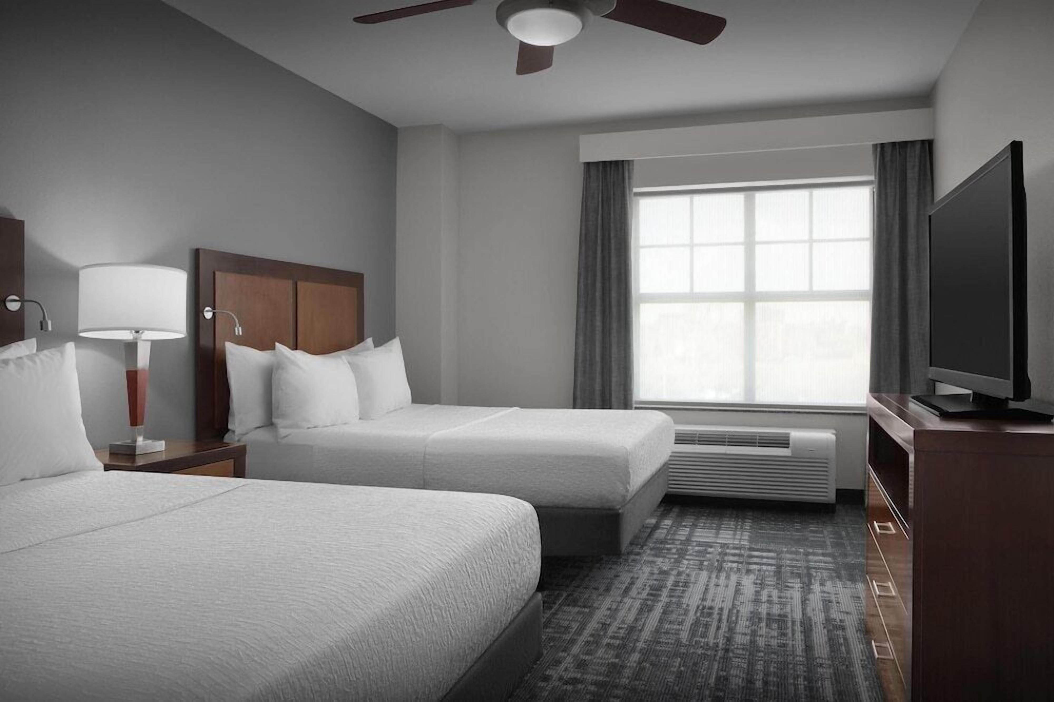 Une chambre d’hôtel avec deux lits, un ventilateur de plafond, une télévision et une grande fenêtre avec des rideaux.