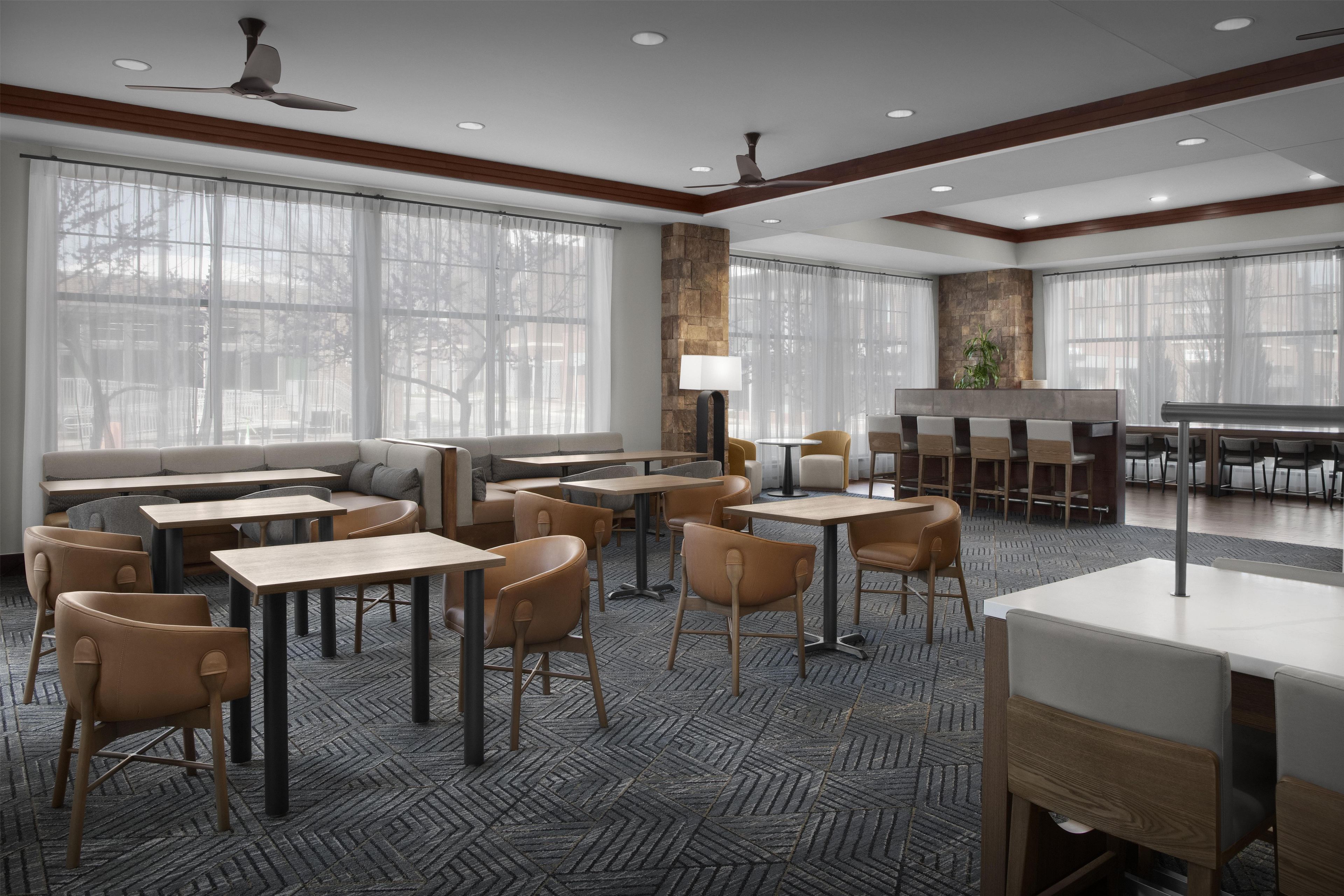 A modern dining area with tables and chairs, large windows, and a stone accent wall.