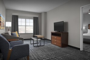 Habitación de hotel con sofá, una mesita, televisor sobre un mueble de madera, una silla y un armario.
