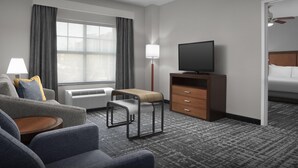 Habitación de hotel con sofá, una mesita, televisor sobre un soporte de madera, calefactor, lámpara y cama con cabecero de madera.