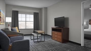 A hotel room with a sofa, a small table, a TV on a wooden stand, a chair, and a wardrobe.