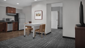 Una cocina moderna con microondas, refrigerador y armarios de madera. Hay una mesa de comedor con dos sillas y un cuadro en la pared.