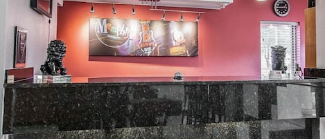 A reception area with a black marble counter, a large wall-mounted TV displaying a music event, and a clock above it.
