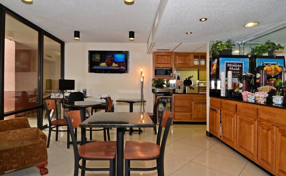 A hotel room with a dining area, a TV mounted on the wall, a kitchen area with a microwave, and a coffee machine.