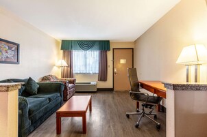 Habitación de hotel con sofá, una mesita, escritorio con silla, ventana con cortinas y puerta.