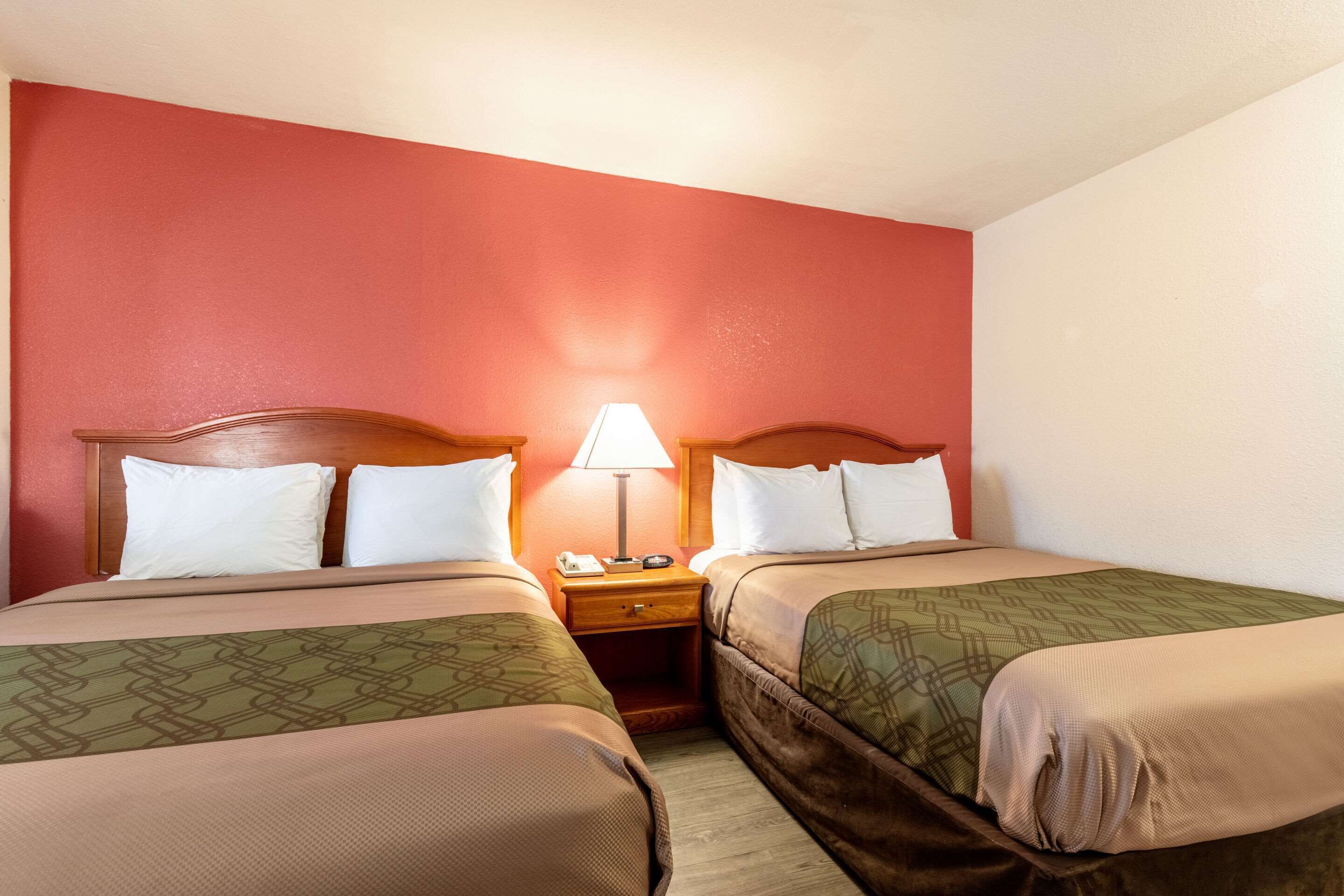 Une chambre d’hôtel avec deux lits, une table de chevet avec une lampe et un mur d’accent rouge.