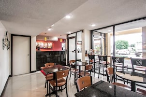 Interior de un restaurante con mesas, sillas, una barra y vista a la calle.
