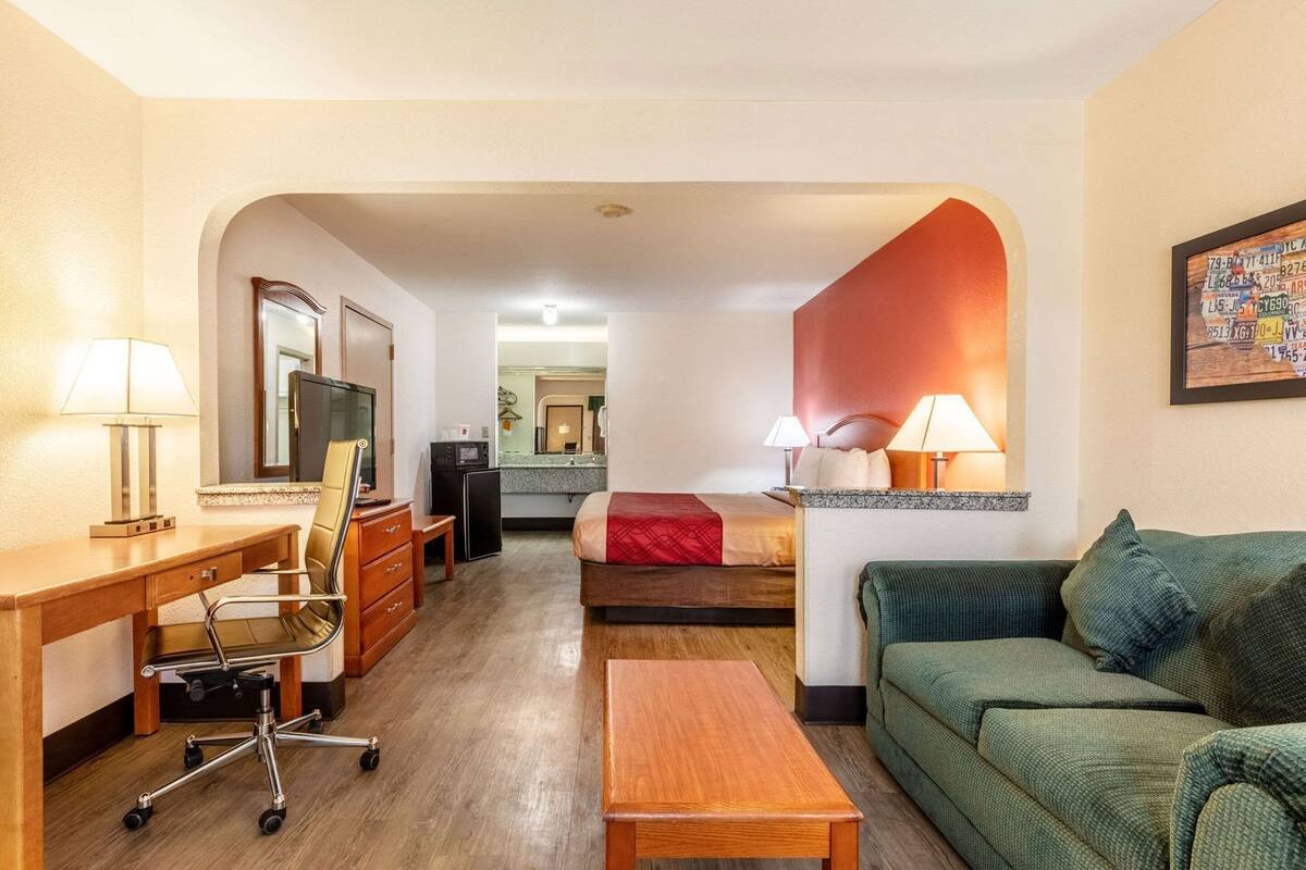 A hotel room with a desk, chair, television, bed, and a green sofa.