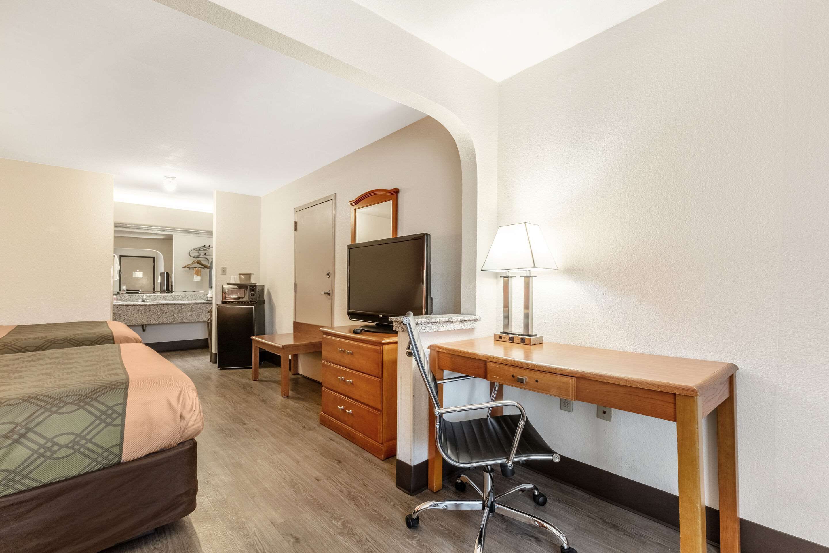 A hotel room with a bed, desk, chair, television, and a mirror.
