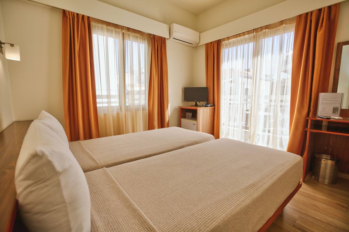 A hotel room with two beds, a desk with a computer, and a window with curtains.