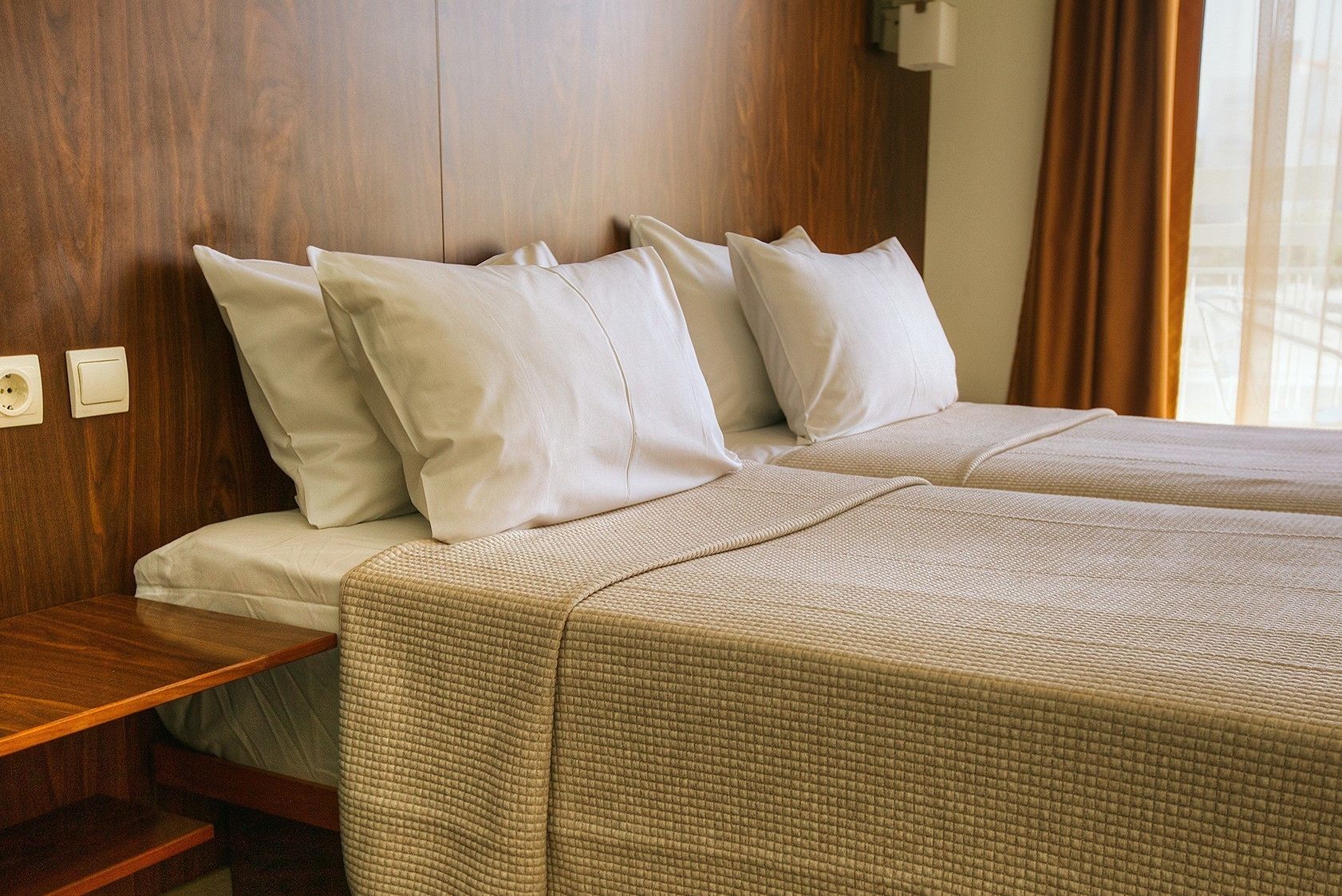 A double bed with a textured beige bedspread, two white pillows, and a wooden headboard.